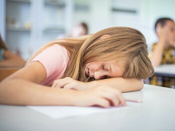 Ein junges Mädchen schläft erschöpft auf ihrem Schreibtisch im Klassenzimmer. 